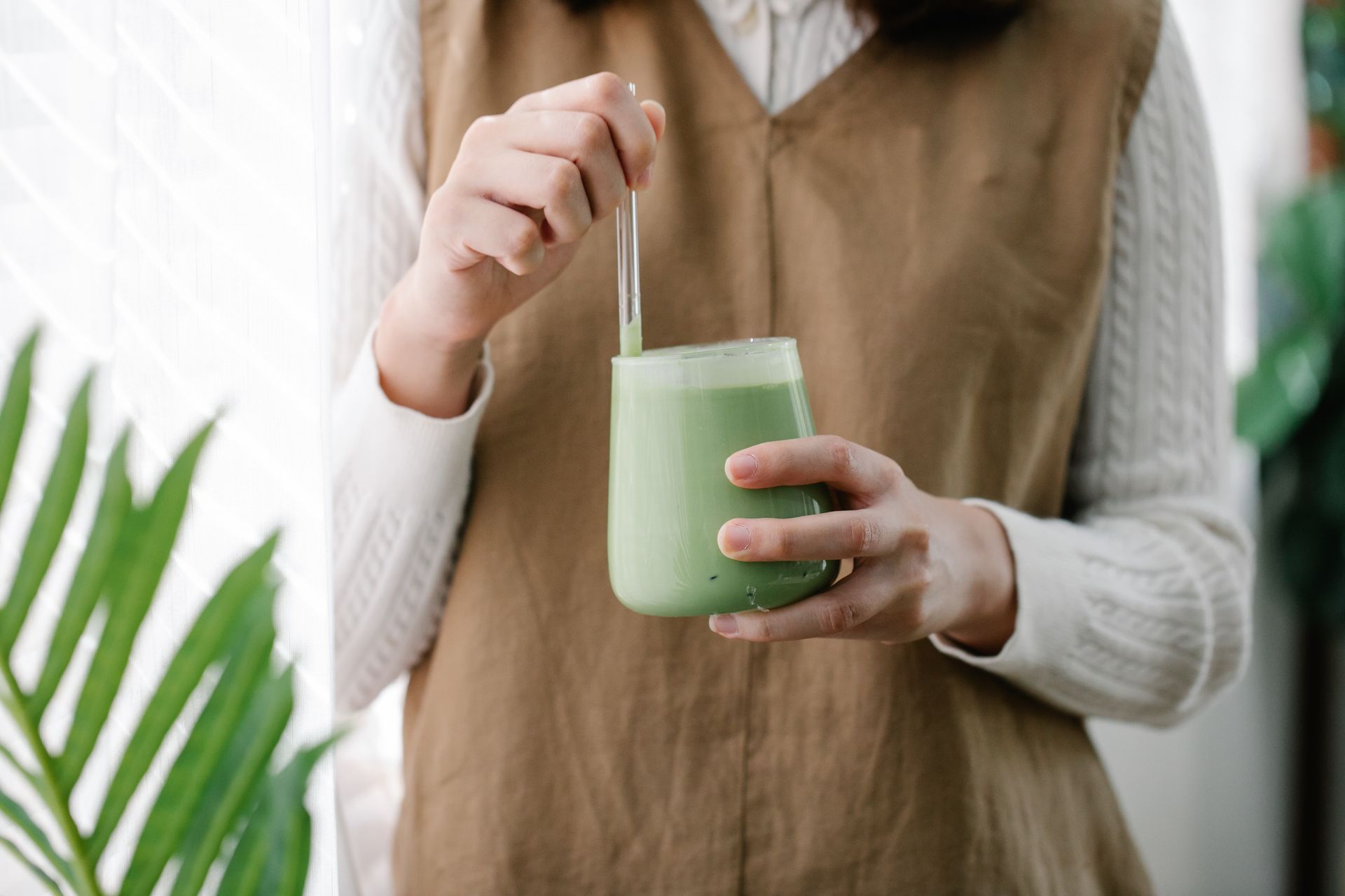 Junge Frau hält ein Glas Matcha mit einem Trinkhalm aus Glasoptik